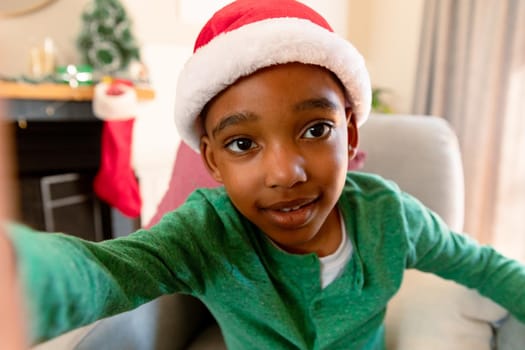 African american boy wearing santa hat and taking selfie at christmas time. christmas, festivity and communication technology.