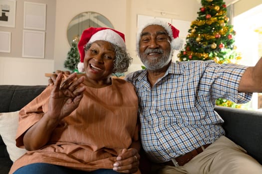 Happy african american couple wearing santa hats having video call at christmas time. christmas, festivity and communication technology at home.