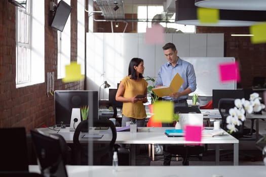 Caucasian male and female colleague discuss tablet and file, view through glass wall and memo notes. working in business at a modern office.