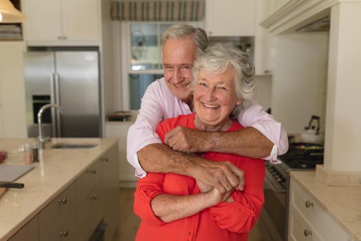 Portrait of senior caucasian couple looking at camera and smiling in kitchen. retreat, retirement and happy senior lifestyle concept.