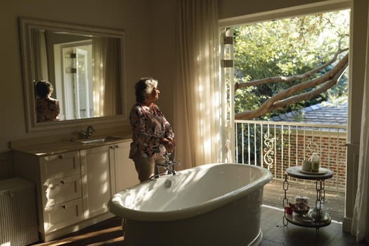 Senior caucasian woman running a bath in bathroom. retreat, retirement and happy senior lifestyle concept.