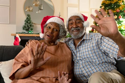 Happy african american couple wearing santa hats having video call at christmas time. christmas, festivity and communication technology at home.