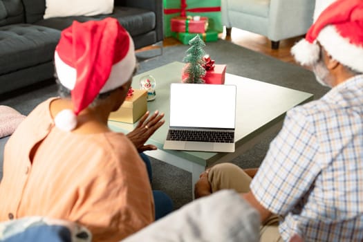 Back view of african american couple using laptop with copy space at christmas time. christmas, festivity and communication technology at home.