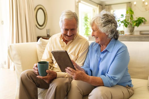 Senior caucasian couple sitting on sofa using tablet. retreat, retirement and happy senior lifestyle concept.