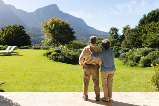 Senior caucasian couple standing and embracing in sunny garden. retreat, retirement and happy senior lifestyle concept.