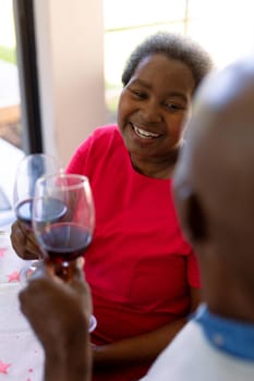 Happy african american senior couple making toast with wine at christmas time. retirement lifestyle and christmas festivities, celebrating at home.