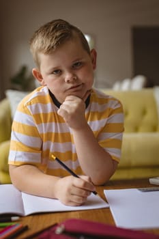 Portrait of caucasian boy holding a pencil sitting in the living room at home. childhood and hobby concept