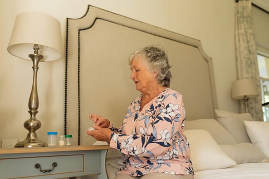 Senior caucasian woman sitting on bed holding taking pills. retreat, retirement and senior lifestyle concept.