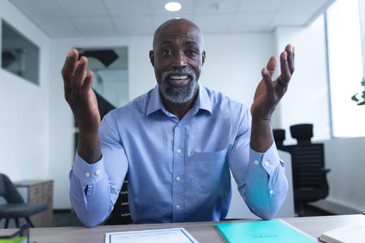 Portrait of african american businessman sitting at desk and having video call. online meeting, working in isolation during quarantine lockdown.