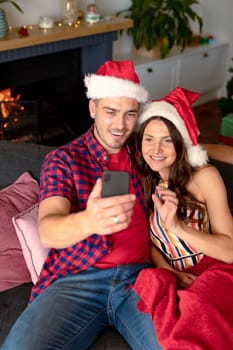 Happy caucasian couple wearing santa hats and having video call on smartphone at christmas time. christmas, festivity and communication technology.