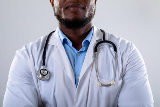 Mid section of african american male doctor against grey background. healthcare and medical professionalism concept