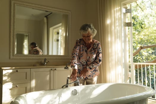 Senior caucasian woman running a bath in bathroom. retreat, retirement and happy senior lifestyle concept.