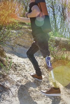 a man on a prosthetic leg travels the mountains. Dressed in black jeans and a T-shirt, he carrying mat.