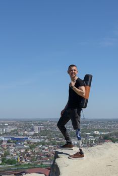 a man on a prosthetic leg travels the mountains. Dressed in black jeans and a T-shirt, he carrying mat.