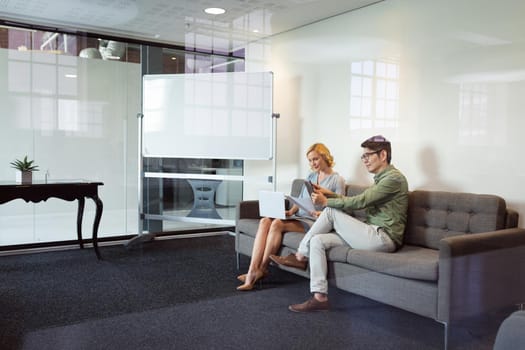 Diverse male and female colleague sitting in office lounge using tablet and laptop. working in business at a modern office.