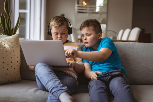 Two caucasian boys using laptop sitting on the couch at home. childhood, technology and home concept