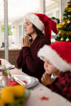 Caucasian boy and his mother praying together at christmas table. family christmas time and festivity together at home.