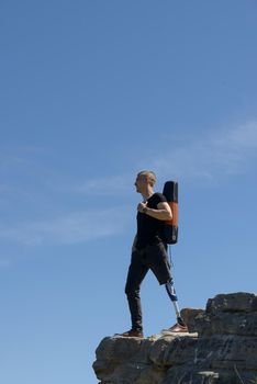 a man on a prosthetic leg travels the mountains. Dressed in black jeans and a T-shirt, he carrying mat.