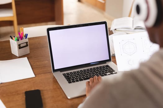 African american young man wearing headphones using laptop with copy space while studying at home. distance learning and online education concept