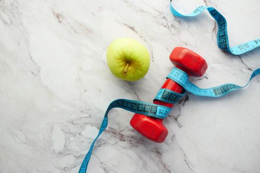 measurement tape apple and a pink color dumbbell on table .