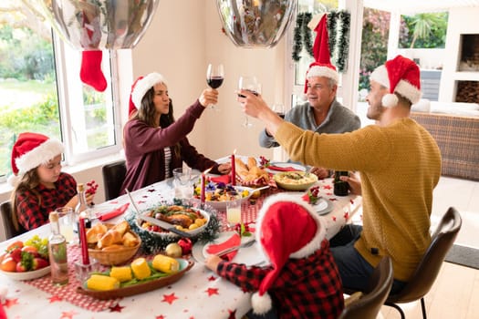 Caucasian multi generation family wearing santa hats having christmas meal, making toast. family christmas time and festivity together at home.
