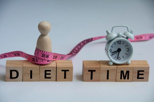 Diet time text on wooden blocks with model wooden doll tied with measuring tape and alarm clock. Weight loss and fitness concept