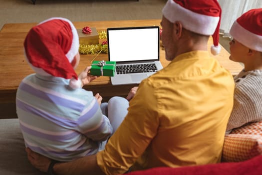 Caucasian father and two sons showing christmas gifts during video call on laptop with copy space. social distancing during covid 19 pandemic at christmas time