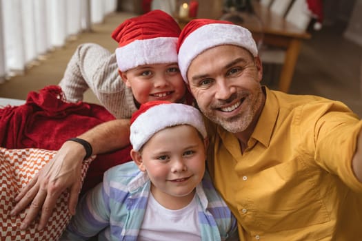 Caucasian father and two sons smiling while talking a selfie at home during christmas. christmas festivity and celebration concept