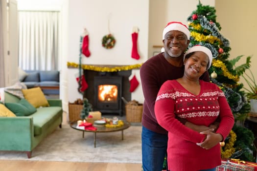 Happy african american senior couple in santa hats taking photo at christmas time. retirement lifestyle and christmas festivities, celebrating at home.
