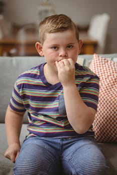 Portrait of caucasian boy making hand gestures sitting on the couch at home. sign language learning concept