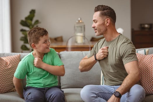 Caucasian father and son communicating using sign language while sitting on the couch at home. sign language learning concept
