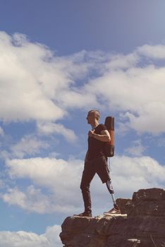 a man on a prosthetic leg travels the mountains. Dressed in black jeans and a T-shirt, he carrying mat.