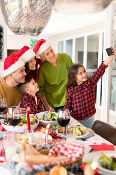 Caucasian multi generation family wearing santa hats taking selfie at christmas time. family christmas time and festivity together at home.