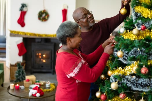 Happy african american senior couple decorating christmas tree at christmas time. retirement lifestyle and christmas festivities, celebrating at home.