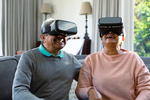 Two happy diverse senior couple wearing vr headset and having fun. retirement lifestyle relaxing at home with technology.