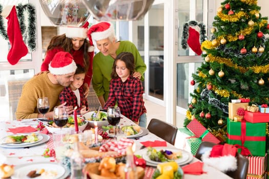 Caucasian multi generation family wearing santa hats looking at smartphone at christmas time. family christmas time and festivity together at home.