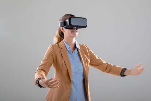 Caucasian businesswoman wearing vr headset widening her arms, isolated on grey background. business, technology, communication and growth concept.
