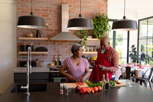 Happy african american senior couple cooking together in kitchen. retirement lifestyle, leisure and spending time at home.