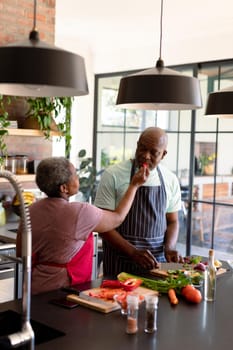 Happy african american senior couple cooking together in kitchen. retirement lifestyle, leisure and spending time at home.