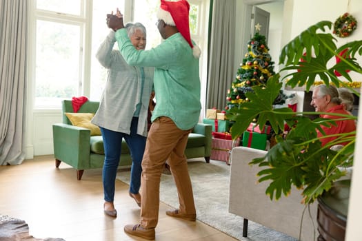 Happy diverse senior couple dancing in living room at christmas time. christmas festivities, celebrating at home with friends.