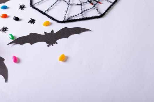 Composition of halloween decorations with spider web, bats and sweets with copy space on white. halloween tradition and celebration concept.