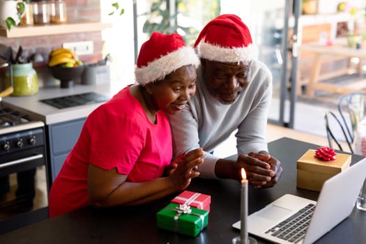 Happy african american senior couple having video call on laptop in kitchen at christmas time. retirement lifestyle, christmas festivities and communication technology.