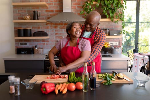 Happy african american senior couple cooking together in kitchen. retirement lifestyle, leisure and spending time at home.