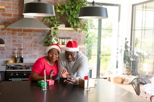 Happy african american senior couple having video call on snartphone in kitchen at christmas time. retirement lifestyle, christmas festivities and communication technology.