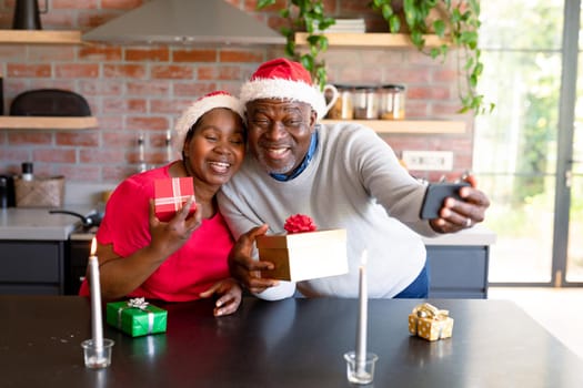 Happy african american senior couple having video call on smartphone in kitchen at christmas time. retirement lifestyle, christmas festivities and communication technology.