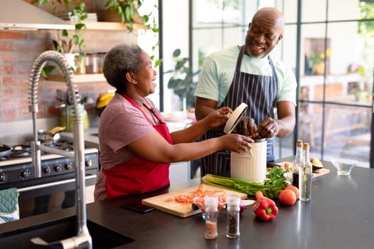 Happy african american senior couple cooking together in kitchen. retirement lifestyle, leisure and spending time at home.