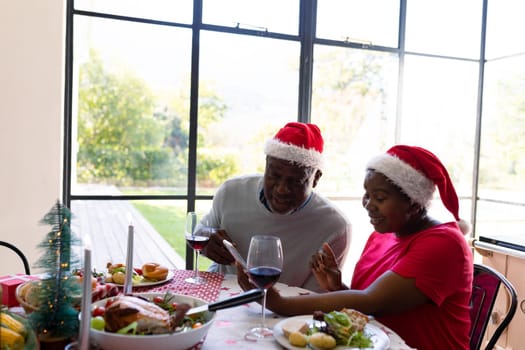 African american senior couple in santa hats using smartphone at christmas time. retirement lifestyle, christmas festivities and communication technology.