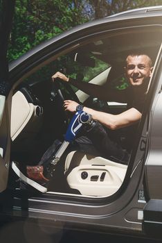 a man on a prosthetic leg sits in a car. Dressed in black jeans and a T-shirt. travel concept, freedom of movement