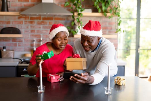 Happy african american senior couple having video call on smartphone in kitchen at christmas time. retirement lifestyle, christmas festivities and communication technology.