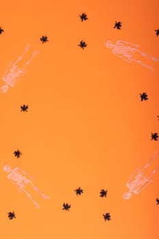 Composition of halloween decorations with black spiders and skeletons on orange background. halloween tradition and celebration concept.